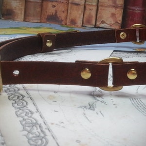 May include: A brown leather belt with gold metal buckles and rivets. The belt is double layered and has a square buckle on one end.