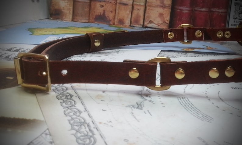 May include: A brown leather belt with gold metal buckles and rivets. The belt is double layered and has a square buckle on one end.