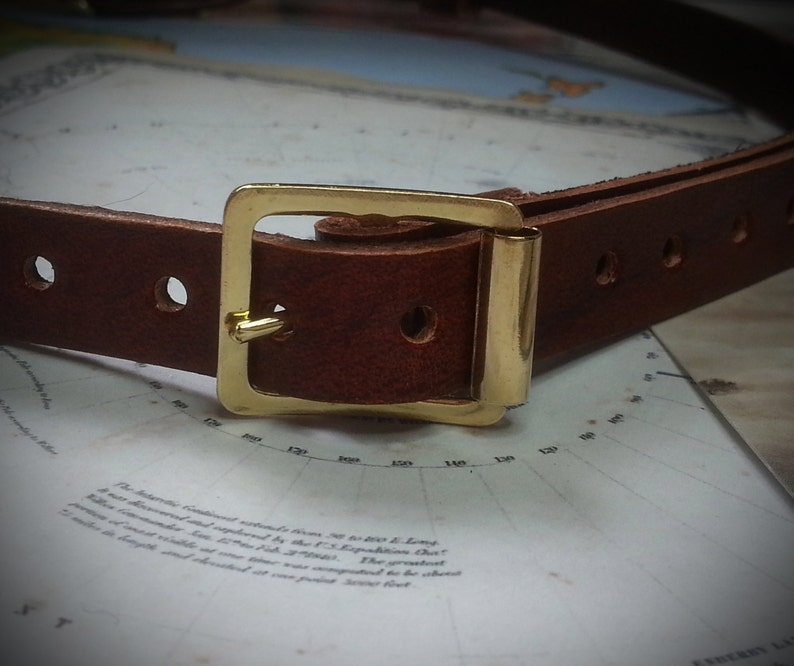 May include: A brown leather belt with a gold metal buckle. The belt has two rows of stitching and a single hole on each side of the buckle.