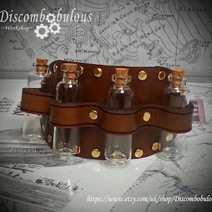 May include: A brown leather belt with six glass vials attached. The belt has gold metal rivets and is decorated with a wavy design. The vials are clear glass with cork stoppers.