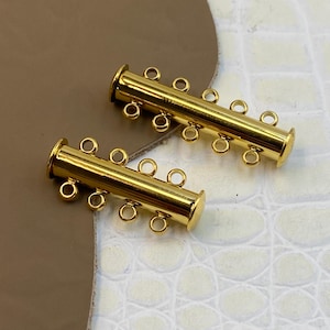 Può includere: Due chiusure a tubo in metallo color oro per la creazione di gioielli. Ogni componente cilindrico presenta una finitura liscia e lucida e include quattro piccoli anelli circolari sul lato per fissare più fili di materiale per gioielli.