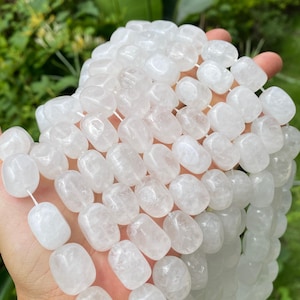 Peut inclure: Un collier de perles en quartz blanc translucide avec une forme rectangulaire arrondie, lisse et polie. Les perles sont enfilées sur un fin cordon blanc, présentant une couleur blanc laiteux uniforme et une texture cristalline semi-opaque.