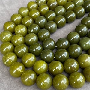 May include: A strand of polished, spherical olive green beads. Each bead features a smooth, glossy surface with subtle variations in color depth, reflecting light across the rounded forms. The beads are arranged in a loose, overlapping cluster.