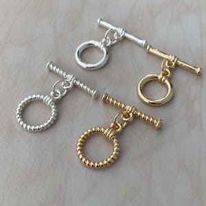 Può includere: Quattro chiusure a T per la creazione di gioielli, incluse due in tonalità argento e due in tonalità oro. Ogni set è composto da un anello circolare e una barra a T. Due chiusure hanno una finitura liscia, mentre le altre due hanno una trama ritorta.