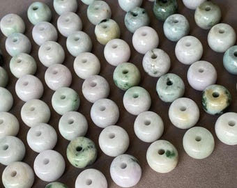 May include: A collection of numerous round, smooth beads with a central hole. The beads feature a variety of light colors, including pale green, white, and soft lavender, with some displaying mottled dark green or grey inclusions throughout.