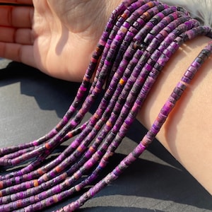 Può includere: Primo piano di fili di perline di pietre preziose viola e rosa. Le perline sono piccole, piatte e rettangolari, con variazioni di colore tra cui nero, arancione e bianco. Le perline sono infilate insieme, creando un aspetto strutturato.