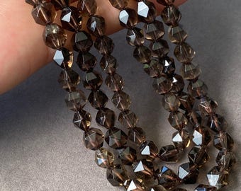 May include: A strand of faceted, translucent dark brown beads with a polished finish. The beads are shaped like small, multi-sided geometric forms, creating a reflective surface that catches light. The strand is arranged in multiple loops.