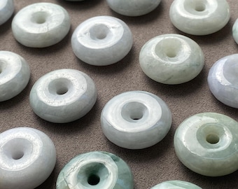 May include: A collection of smooth, polished jade stone beads shaped like small donuts or rings. Each bead features a central circular hole and displays natural variations in pale green, white, and soft grey tones with a glossy finish.