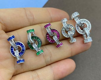 May include: Five metal earrings featuring a circular design adorned with baguette-cut stones. The earrings are available in blue, green, magenta, and two clear white variations, each showcasing a linked structure with a vertical bar.