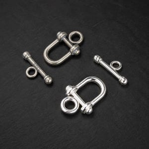 May include: Two silver-toned toggle clasps, each consisting of a U-shaped shackle component and a T-bar component. One T-bar is clearly stamped with the text S925. The metal pieces have a polished finish and are designed for jewelry assembly.