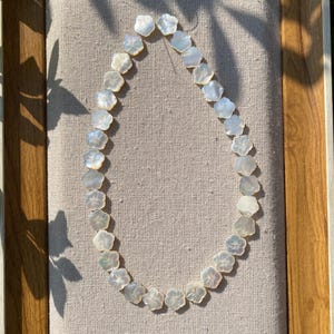 Peut inclure: Un collier délicat composé de perles en forme de fleurs. Les perles sont d'un blanc nacré et sont enfilées pour former le collier. Le collier est présenté sur un tissu de couleur neutre.