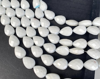 May include: Close-up of white, faceted teardrop-shaped beads. The beads are strung together, creating multiple strands. The beads have a glossy finish and are arranged against a dark background. The beads are likely for jewelry making.