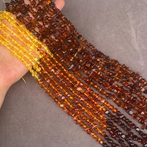 Puede incluir: Múltiples hilos de pequeñas cuentas de piedras preciosas pulidas e irregulares dispuestas en un patrón de degradado. Las cuentas pasan de un amarillo brillante y translúcido a un marrón oscuro profundo, mostrando tonos cálidos.