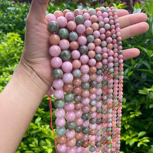 Può includere: Fili di perline di pietre preziose in varie dimensioni e colori, tra cui rosa, verde e marrone. Le perline rotonde sono infilate su un cordoncino rosa, adatte per la creazione di gioielli o progetti di artigianato.