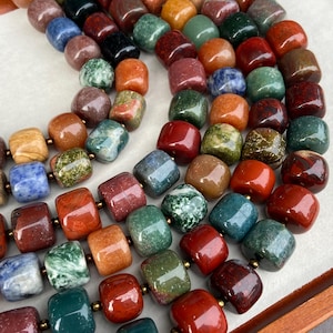 May include: A collection of polished, multi-colored gemstone beads arranged in several strands. The beads are square-shaped with rounded edges, featuring a variety of natural stone patterns in shades of red, green, blue, orange, and brown.