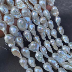 Puede incluir: Colección de perlas blancas barrocas. Las perlas tienen una superficie iridiscente y formas irregulares. Están ensartadas, probablemente para joyería. Cada perla mide aproximadamente 1-2 cm de largo.