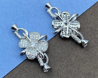 May include: Two silver-toned jewelry clasps shaped like four-leaf clovers, each encrusted with numerous small clear stones and featuring a central larger clear stone, with integrated loops for attaching to necklaces or bracelets.