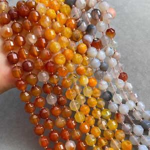 May include: Multiple strands of faceted, round gemstone beads in a gradient of colors ranging from deep burnt orange and amber to translucent white and soft gray. Each bead features a polished, multi-faceted surface reflecting light.