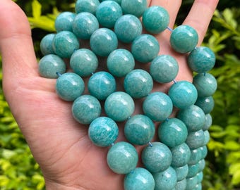 May include: A strand of turquoise-colored gemstone beads. The beads are round and have a polished, glossy finish. The beads are strung together on a blue string. The beads are held in a hand.
