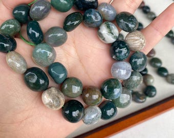May include: A strand of polished moss agate beads in various shades of deep forest green, translucent gray, and creamy white. The beads are smooth, rounded, and irregular in shape, strung together on a thin green cord, showcasing natural inclusions.