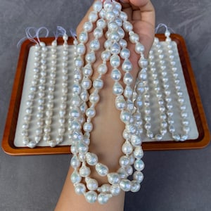 Può includere: Una collezione di fili di perle barocche bianche caratterizzate da forme irregolari e organiche con una finitura molto lucida. Ogni filo è infilato su un sottile cordino bianco, mettendo in risalto le variazioni naturali e il riflesso.