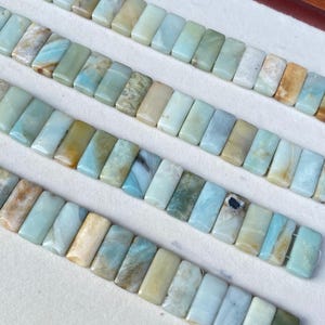Pode incluir: Fileiras de contas retangulares de pedra preciosa Amazonita em tons de azul, verde e bege. As contas são enfiadas, mostrando as variações naturais de cor e padrão. Ideal para fazer joias.