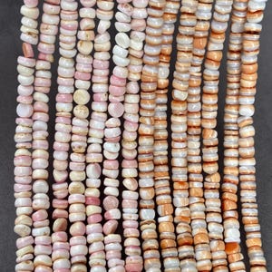 May include: Multiple vertical strands of small, disc-shaped beads made from natural shell. The beads feature a color palette of soft pink, creamy white, and warm orange tones, with each individual bead displaying unique variations in texture and opacity.