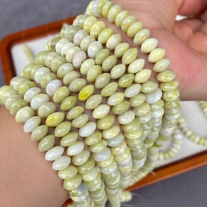 Peut inclure: Une collection de perles ovales vert clair enfilées sur plusieurs fils. Les perles ont une finition lisse et polie avec de subtiles variations de couleur, allant du jaune-vert pâle au blanc doux, créant une apparence uniforme.