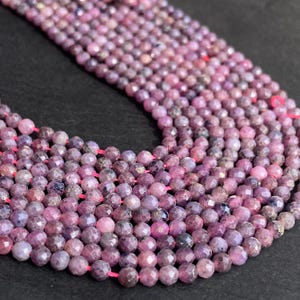 May include: Strands of faceted, round, purple-pink gemstones. The beads are strung on a pink cord, creating a necklace or bracelet component. The gemstones have a sparkling, polished appearance, and vary in shades of purple and pink.