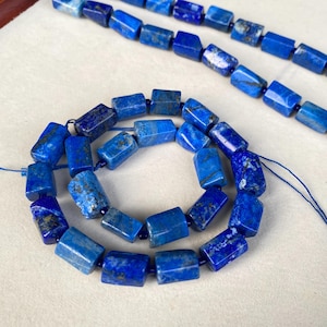 May include: Strands of vibrant blue lapis lazuli beads. The beads are rectangular with a polished finish, showcasing natural variations in color and texture. The beads are strung together, ready for jewelry making.