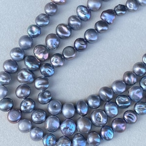 Könnte beinhalten: Nahaufnahme von mehreren Strängen irisierender grauer Süßwasserperlen. Die Perlen haben einen glänzenden Glanz und variieren in Größe und Form, wobei einige runder und andere unregelmäßiger sind. Der Hintergrund ist hell und neutral.