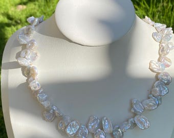 May include: A necklace composed of numerous irregular, white, lustrous freshwater pearls. Each pearl features a unique, organic shape with a high-gloss finish that reflects light, creating a shimmering effect across the entire strand.