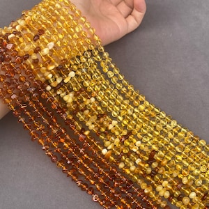 Puede incluir: Múltiples hilos de cuentas de ámbar pulidas en varios tonos de amarillo, dorado y marrón oscuro. Las cuentas son pequeñas, redondeadas y de forma irregular, ensartadas para formar largos collares en cascada con un acabado liso y translúcido.
