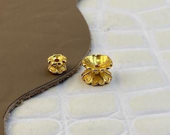 May include: Two gold-toned metal bead caps with a scalloped edge design. Each piece features a central hole and a flared, flower-like shape. The components are metallic gold in color with a textured finish, showing a smaller and a larger size.