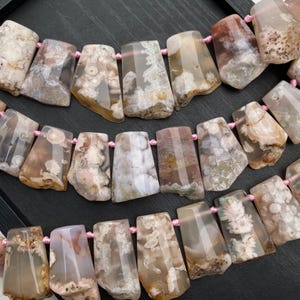 May include: Strands of agate gemstone beads in shades of beige, brown, and white. The rectangular beads are strung on pink cord. The natural stone has unique patterns and textures, creating a beautiful and organic look. Ideal for jewelry making.