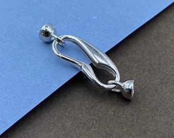 May include: A silver-toned jewelry clasp featuring a smooth, elongated oval frame with a spring-loaded mechanism. The clasp includes two small, rounded end caps attached to each side, designed for securing necklaces or bracelets with a polished finish.