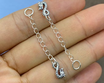 May include: Two silver-toned metal chain extenders, each featuring a small, detailed dragon charm at one end and a circular jump ring at the other. The chains consist of oval-shaped links, providing a flexible connection for jewelry pieces.