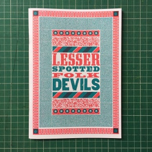 Puede incluir: Un póster blanco con un borde de patrón geométrico de color azul verdoso y rojo. El texto "Lesser Spotted Folk Devils" está en letras rojas y azul verdoso.