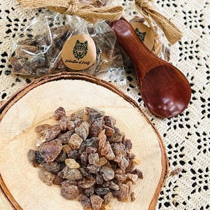 May include: A small wooden spoon sits next to a bag of brown sugar crystals. The bag is tied with twine and has a label that says "Woodland Wolf".