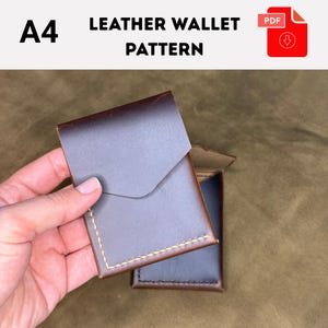 May include: A brown leather wallet with a flap closure, held in a hand. The wallet has a stitched border and is shown with a second wallet. The text "A4 LEATHER WALLET PATTERN" is at the top.