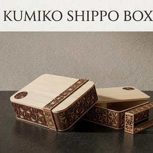 Peut inclure: Boîtes Kumiko Shippo en bois avec des motifs géométriques complexes. Les boîtes sont de couleur claire avec des accents marron foncé, avec un couvercle et une base séparée. Le texte "KUMIKO SHIPPO BOX" est affiché en haut.