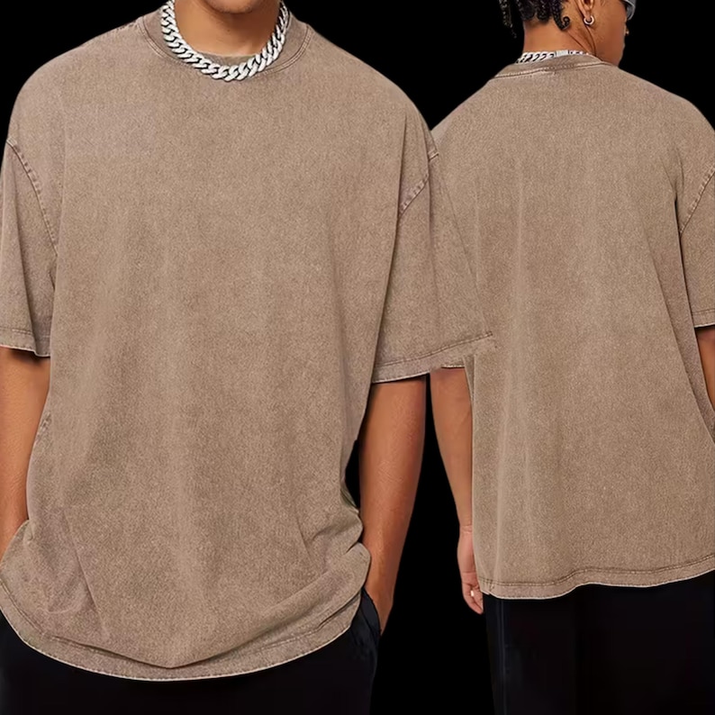 A person wearing a beige t-shirt and black pants, with a silver chain necklace visible.