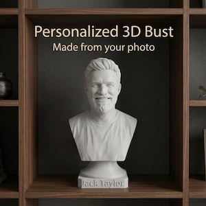 Pode incluir: Um busto impresso em 3D branco mate de uma pessoa com cabelo curto e cavanhaque, vestindo uma t-shirt. A base do busto apresenta o texto gravado "Jack Taylor". Acima do busto, o texto diz "Personalized 3D Bust Made from your photo".