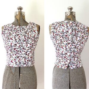 May include: A sleeveless white top with a floral print in shades of red, blue, and yellow. The top has a button closure in the back.