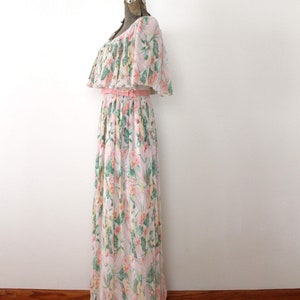 May include: A long, white maxi dress with a pink floral print and a ruffled neckline. The dress has a pink sash at the waist and a tiered skirt.