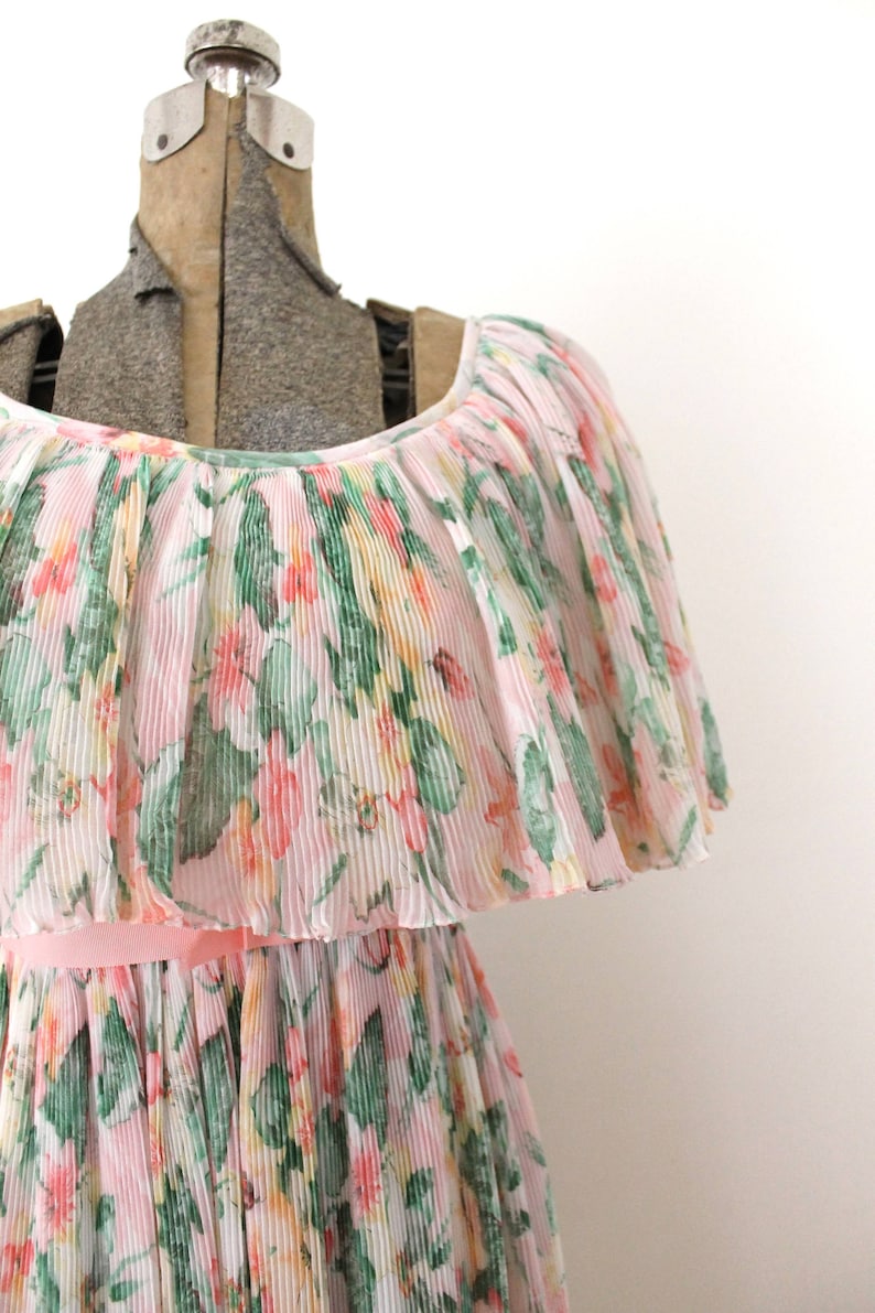 May include: A pink and white floral dress with a ruffled neckline and a pleated skirt. The dress is made of a lightweight fabric and has a delicate floral print.