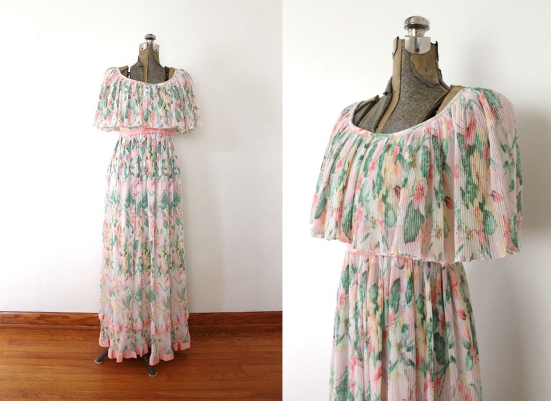 May include: A long, white maxi dress with a floral print in shades of pink, green, and yellow. The dress has a ruffled neckline and a cinched waist.