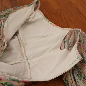 May include: A floral print dress with a white lining. The dress has a zipper closure and long sleeves.
