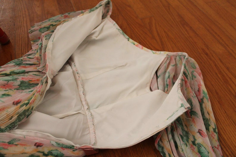May include: A floral print dress with a white lining. The dress has a zipper closure and long sleeves.