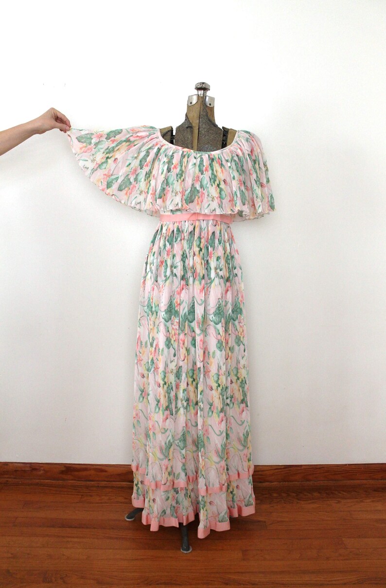May include: A long, pink and white floral print dress with a ruffled off-the-shoulder neckline and a pink ribbon belt. The dress has a tiered skirt with pink ruffles at the hem.